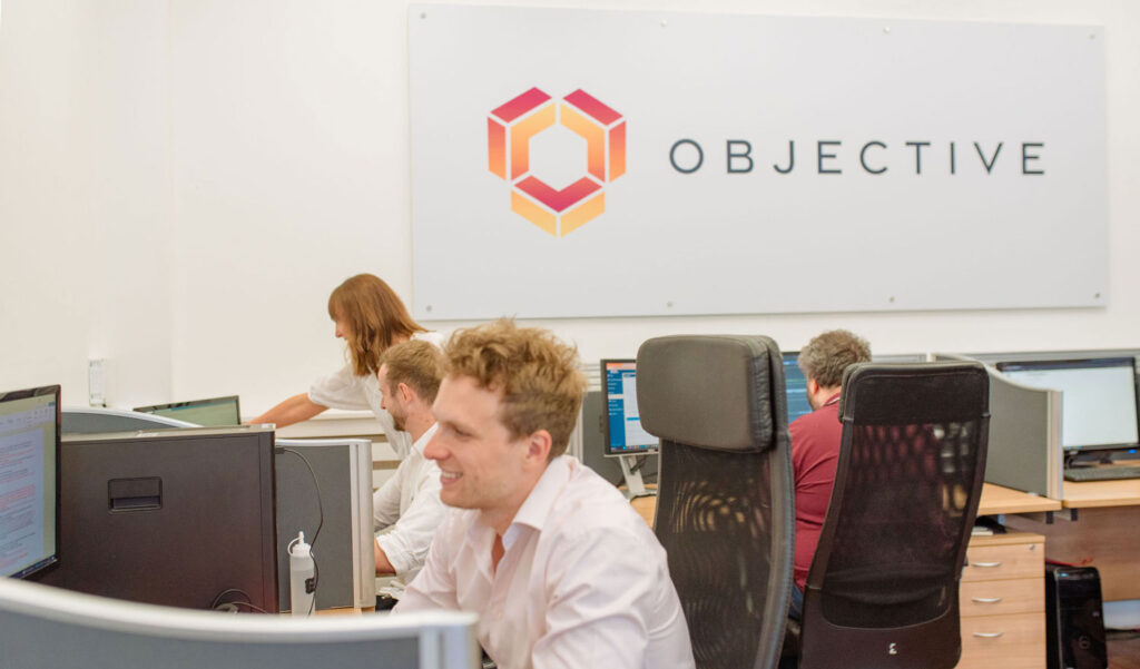 Objective Database Developers at their Essex office. White walls with their logo and team mambers working on screens