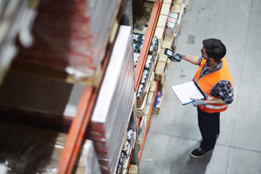 man in a warehouse wearing an orange hi-vis jacket doing a stock check with Intelligent Process Automation (IPA)