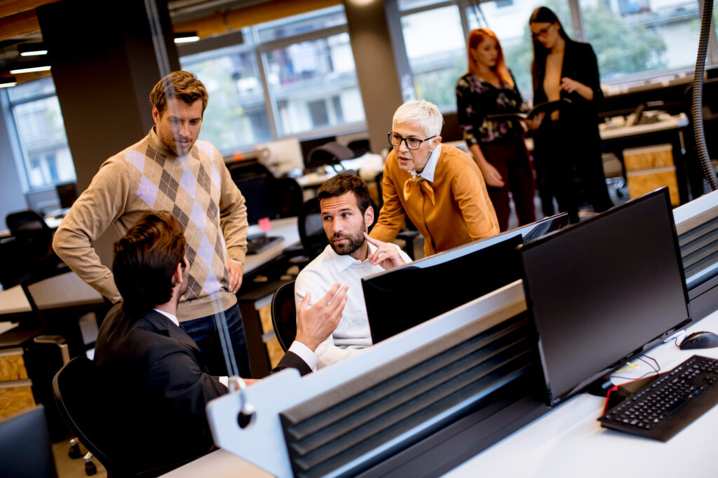 business team around a screen in a large darkly lit office. 1 women and 2 men as part of an IT department of azure management