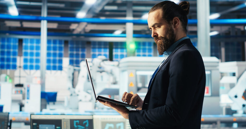 business owner on a factory floor holding a laptop using a power platform for business